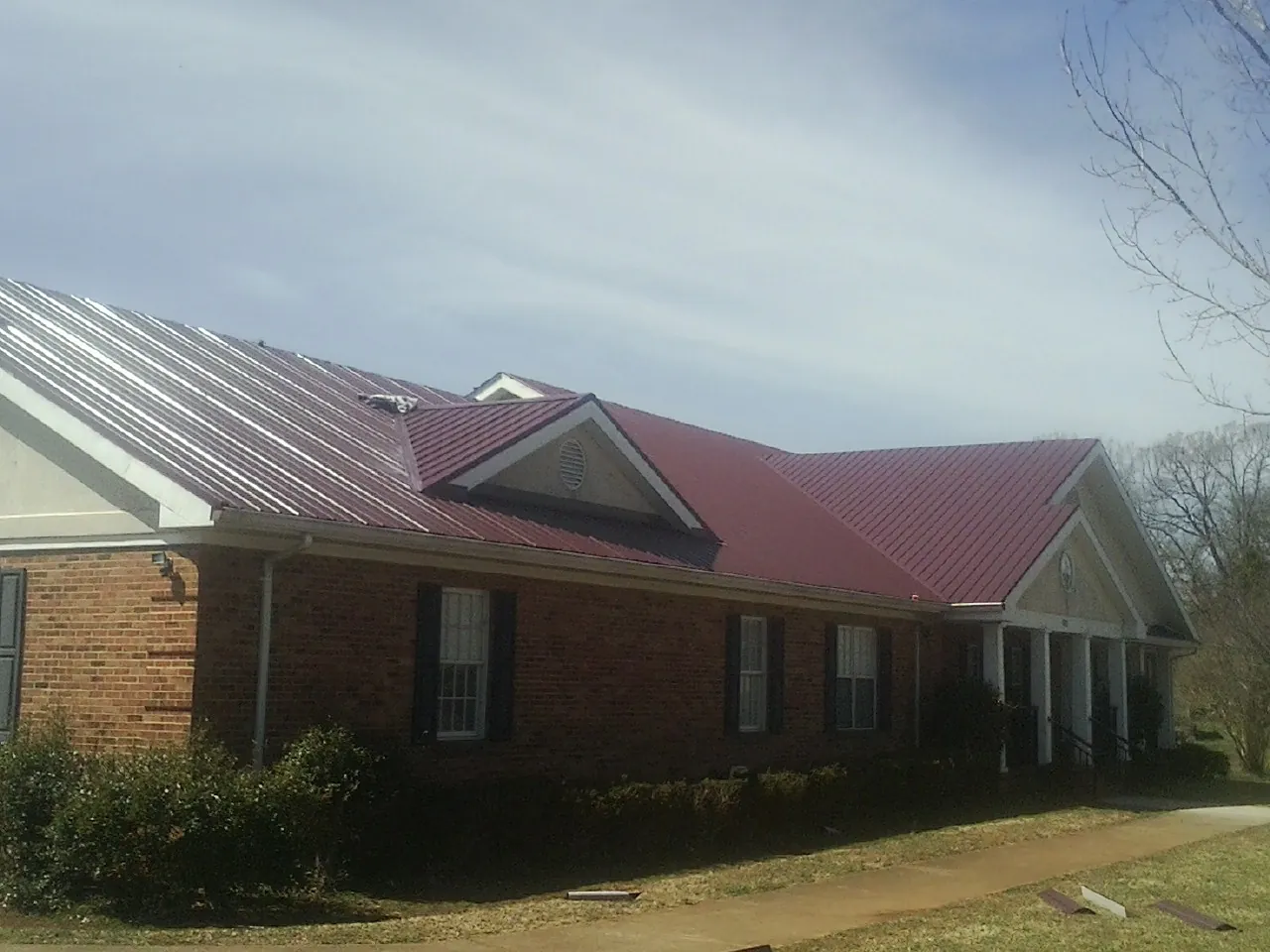 Red metal roof with gabled entries on a long brick building, from a Hail Damage Roof Repair job in Lowellville