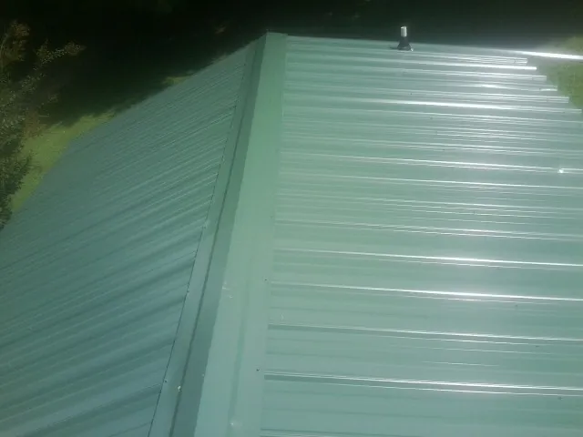 New green metal panels meeting at the ridge of a roof — Flat Roof Repair work by our crew in Lowellville