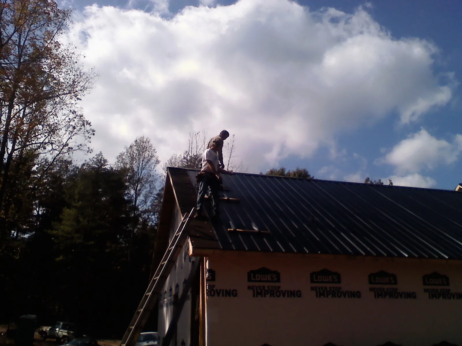 Roofer fastening dark metal panels high against a cloudy sky, from a Roof Inspection job in Lowellville