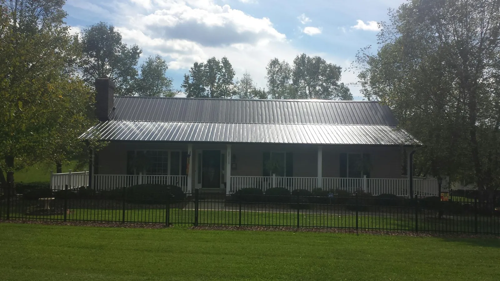 Gray metal roof on a brick ranch with a full width front porch — Gutter Guard Installation work by our crew in Lowellville
