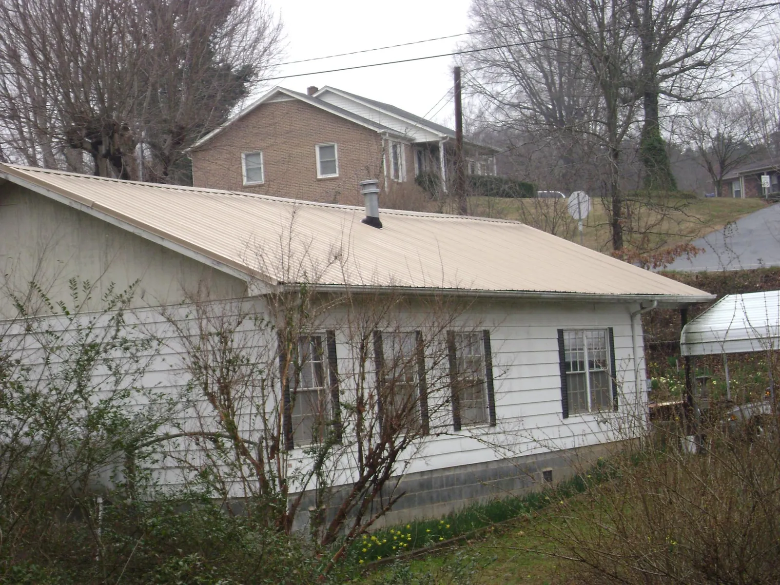 Tan metal roof on a white sided house set into a hillside — Commercial Roofing by Roofing Brothers in Lowellville